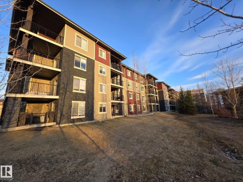 Multi-story building featuring balconies with black railings, horizontal siding in multiple colors, and a stone facade - #206 12045 22 Av Sw, Edmonton, AB 