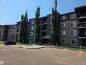 Multi-story building featuring stone-clad and panel siding accents, multiple private balconies, and a paved parking area - #206 12045 22 Av Sw, Edmonton, AB 
