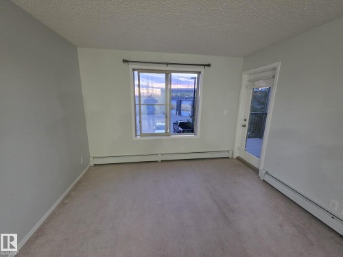 Carpeted flooring, single pane window, exterior door with glass insert, wall-mounted heating units - #206 12045 22 Av Sw, Edmonton, AB 