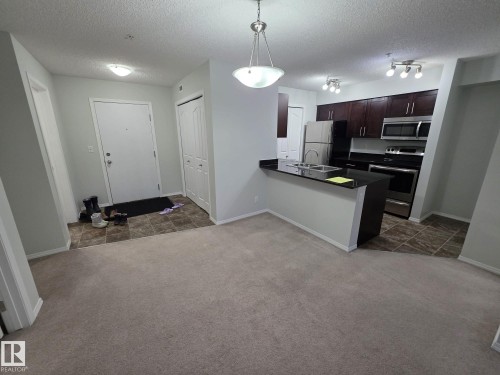 Kitchen featuring dark wood cabinetry, stainless steel appliances, and a breakfast bar with a double basin sink - #206 12045 22 Av Sw, Edmonton, AB 