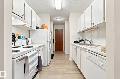 Galley kitchen featuring white cabinetry, wood-finish flooring, white tile backsplash, and recessed lighting - #1507 9835 113 St Nw, Edmonton, AB 