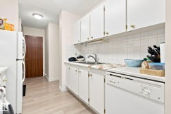 Kitchen featuring white cabinetry with gold-tone hardware, white appliances, light wood-finish flooring, and a tiled backsplash - 