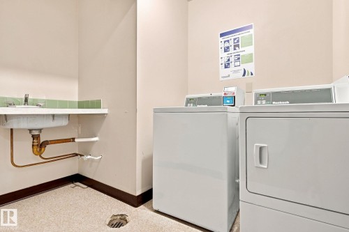 Functional utility space featuring a laundry sink with visible plumbing, two white laundry machines, and light-toned flooring - #1507 9835 113 St Nw, Edmonton, AB 