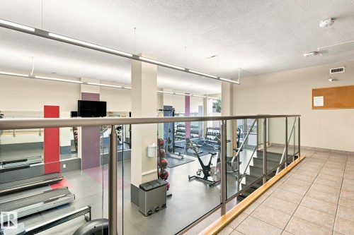 Fitness area featuring a glass and metal railing, tile flooring, and stairs with metal handrails - #1507 9835 113 St Nw, Edmonton, AB 