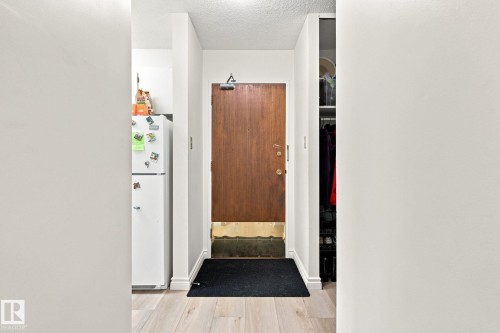 Entryway featuring wood-finish flooring, a solid wood door, and an integrated storage closet - #1507 9835 113 St Nw, Edmonton, AB 