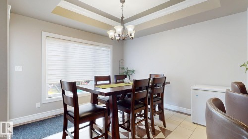 Tray ceiling with recessed lighting, large window with blinds, tile flooring, and a chandelier light fixture - 1232 Cunningham Drive Sw, Edmonton, AB 