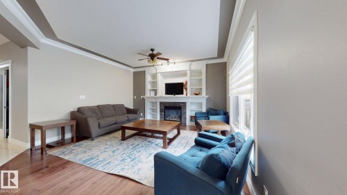Living area featuring wood-finish flooring, a tray ceiling with crown molding, and a built-in fireplace with shelving - 1232 Cunningham Drive Sw, Edmonton, AB 
