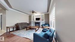Living area featuring wood-finish flooring, a tray ceiling with crown molding, and a built-in fireplace with shelving - 