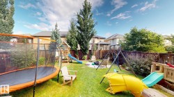 Expansive backyard featuring a lush lawn, privacy fencing, mature trees, and a wooden play structure - 