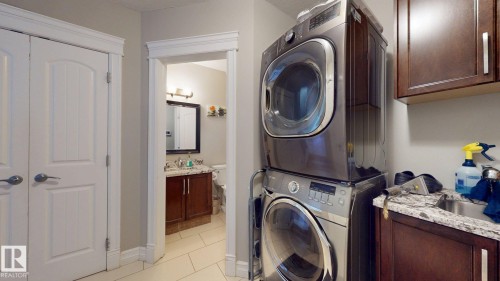 Laundry area featuring a stacked washer and dryer, wood-finish cabinetry, and a utility sink with a stone-look countertop - 1232 Cunningham Drive Sw, Edmonton, AB 