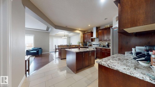 Kitchen featuring wood cabinetry, light-colored tile flooring, granite countertops, and stainless steel appliances - 1232 Cunningham Drive Sw, Edmonton, AB 