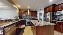 Kitchen featuring rich wood cabinetry, stone countertops, a tile backsplash, stainless steel appliances, and a central island - 
