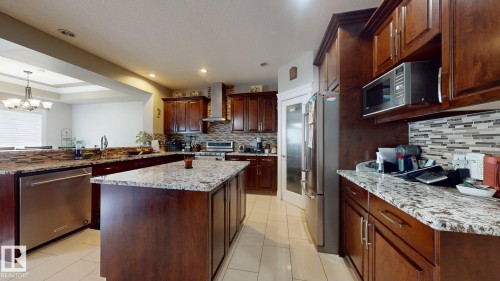 Kitchen featuring wood-finish cabinetry, stainless steel appliances, granite countertops, and a tile backsplash - 1232 Cunningham Drive Sw, Edmonton, AB 