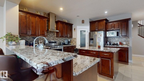 Kitchen featuring wood cabinetry, stainless steel appliances, a large island with a bar seating extension, and stone countertops - 1232 Cunningham Drive Sw, Edmonton, AB 