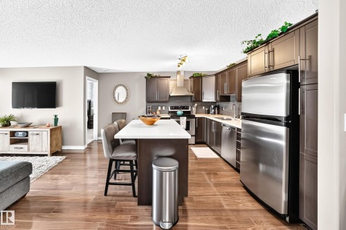 Kitchen featuring stainless steel appliances, dark wood-finish cabinetry, and a light-toned countertop island - #418 279 Suder Greens Dr Nw, Edmonton, AB 