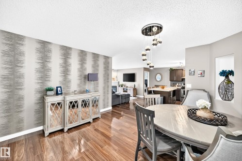 Wood-finish flooring, accent wall with textured wallpaper, recessed wall niche, and an open-concept living area - #418 279 Suder Greens Dr Nw, Edmonton, AB 