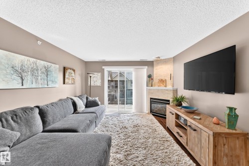 Corner fireplace with a stone surround, glass sliding door, and wood-finish flooring - #418 279 Suder Greens Dr Nw, Edmonton, AB 