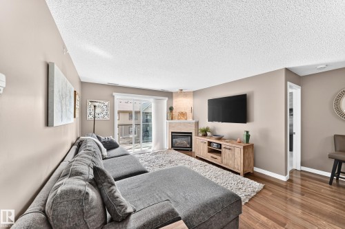 Wood-finish flooring, sliding glass door, built-in fireplace, light neutral wall color - #418 279 Suder Greens Dr Nw, Edmonton, AB 