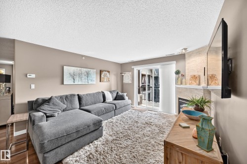 Living area featuring a fireplace with a stone surround, a white mantel, and wood-finish flooring - #418 279 Suder Greens Dr Nw, Edmonton, AB 