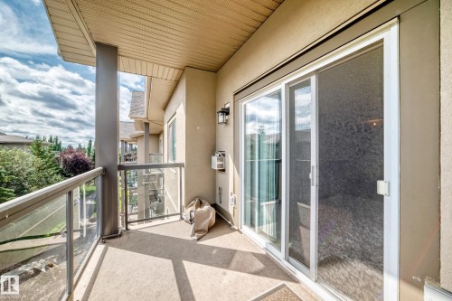 Private balcony featuring a glass railing, sliding glass door, and exterior wall sconce - #418 279 Suder Greens Dr Nw, Edmonton, AB 