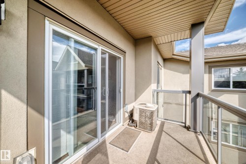 Balcony featuring glass panel railings, textured exterior walls, and a sliding glass door - #418 279 Suder Greens Dr Nw, Edmonton, AB 