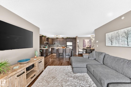 Open-concept design featuring wood-finish flooring, recessed lighting, and a modern kitchen with dark cabinetry and stainless steel appliances - #418 279 Suder Greens Dr Nw, Edmonton, AB 