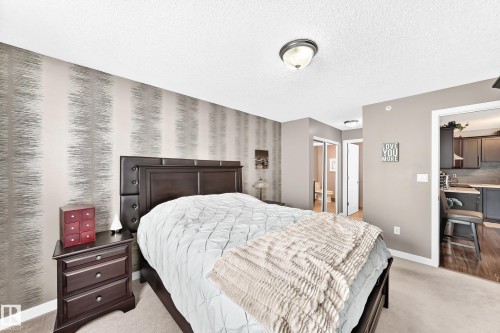 Textured accent wall, ceiling-mounted light fixture, light-colored carpeting, dark wood-finish flooring in adjacent space, dark cabinetry in adjacent space - #418 279 Suder Greens Dr Nw, Edmonton, AB 