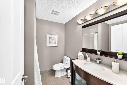 Curved dark wood vanity with a light-toned countertop, oval undermount sink, and polished chrome faucet - #418 279 Suder Greens Dr Nw, Edmonton, AB 