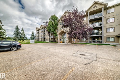 Multi-story building featuring balconies with glass railings, an inviting main entrance, and an expansive parking area - #418 279 Suder Greens Dr Nw, Edmonton, AB 