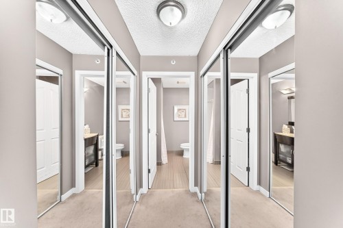 Hallway featuring mirrored sliding closet doors, flush mount lighting, and wood-finish flooring visible through doorways - #418 279 Suder Greens Dr Nw, Edmonton, AB 