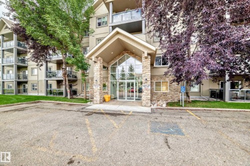 Building exterior featuring a stone-clad entrance, expansive glass doors, and multiple private balconies with glass railings - #418 279 Suder Greens Dr Nw, Edmonton, AB 
