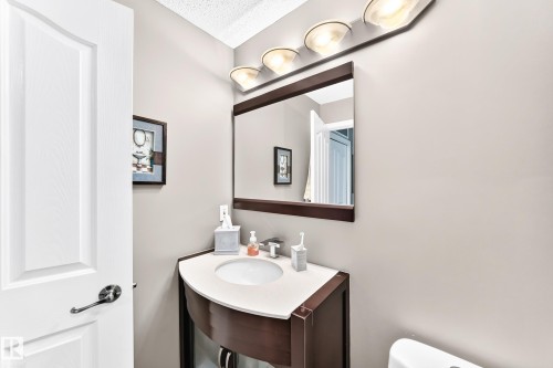 White paneled door with polished hardware, wall-mounted vanity lighting, framed mirror, curved vanity with integrated sink, and light-toned walls - #418 279 Suder Greens Dr Nw, Edmonton, AB 
