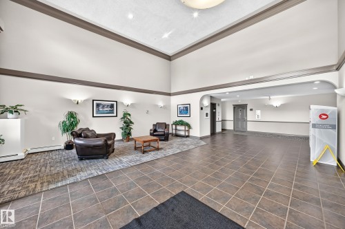Spacious common area featuring high ceilings, tile flooring, wall sconce lighting, and a broad archway - #418 279 Suder Greens Dr Nw, Edmonton, AB 