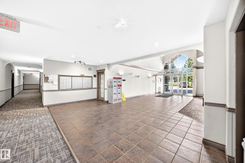 Tiled flooring entry, glass-paneled double doors, vaulted glass ceiling, built-in mailboxes, and recessed lighting - #418 279 Suder Greens Dr Nw, Edmonton, AB 