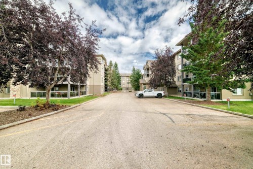 Multi-story residential buildings featuring balconies with glass railings, surrounding a paved parking area - #418 279 Suder Greens Dr Nw, Edmonton, AB 