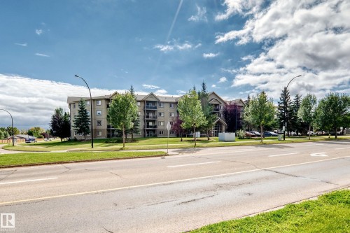 Multi-story residential building featuring private balconies, pitched roofline, and landscaped perimeter with mature trees - #418 279 Suder Greens Dr Nw, Edmonton, AB 