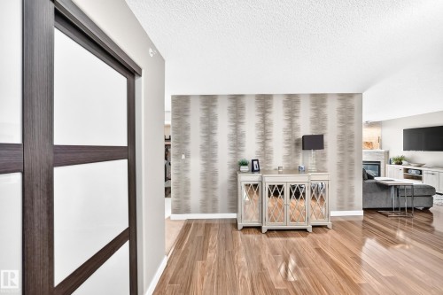 Hardwood-finish flooring throughout, accent wall with patterned wallpaper, and a dark wood-frame sliding door - #418 279 Suder Greens Dr Nw, Edmonton, AB 
