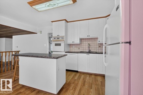 Kitchen featuring wood-finish flooring, white cabinetry, dark countertops, a built-in oven, and a central island with a contrasting dark countertop - 4027 74 Street Nw, Edmonton, AB - Indoor Photo Showing Kitchen