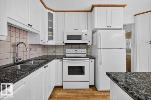 Kitchen featuring white cabinetry, dark speckled countertops, and wood-finish flooring - 4027 74 Street Nw, Edmonton, AB - Indoor Photo Showing Kitchen With Double Sink