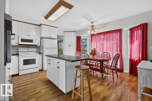 Kitchen featuring white cabinetry, dark countertops, wood-finish flooring, white appliances, and a central island - 4027 74 Street Nw, Edmonton, AB - Indoor Photo Showing Kitchen