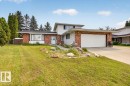 Split-level residence featuring a brick and white siding facade, an attached garage with a concrete driveway, and a front lawn with mature trees and established landscaping - 4027 74 Street Nw, Edmonton, AB  - Outdoor With Facade 