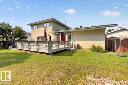 Expansive rear yard featuring a large elevated deck, stucco exterior, multiple windows, and a storage shed - 4027 74 Street Nw, Edmonton, AB - Outdoor