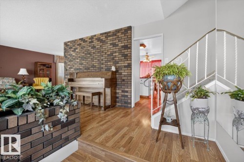 Interior entryway featuring wood-finish flooring, a brick accent wall, and a white metal staircase railing - 4027 74 Street Nw, Edmonton, AB - Indoor Photo Showing Other Room