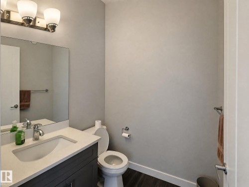 Vanity with an integrated sink and light-toned countertop, dark wood-finish flooring, wall-mounted mirror, and a two-bulb vanity light fixture - 13309 128 Street Nw, Edmonton, AB 