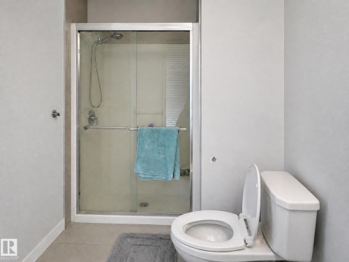 Glass-enclosed shower with a chrome shower head and handle, white tile surround, and a white toilet - 13309 128 Street Nw, Edmonton, AB 