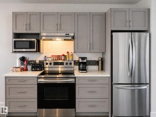 Contemporary kitchen featuring grey shaker-style cabinetry, stainless steel appliances, white subway tile backsplash, and light-toned countertops - 13309 128 Street Nw, Edmonton, AB 