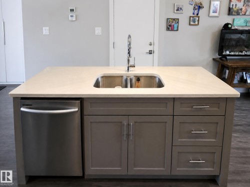 Kitchen island featuring a dual basin stainless steel sink, a pull-down faucet, a built-in dishwasher, and shaker-style cabinetry with drawers - 13309 128 Street Nw, Edmonton, AB 