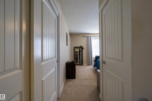 Carpeted hallway with white paneled doors and textured ceilings - #75 8315 180 Av Nw, Edmonton, AB 