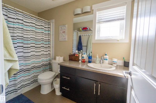 Bathroom featuring a dark wood-finish vanity with an undermount sink, a window, wall-mounted sconces, and neutral wall tones - #75 8315 180 Av Nw, Edmonton, AB 