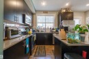 Modern kitchen featuring dark wood-finish cabinetry, stainless steel appliances, a built-in microwave, and wood-finish flooring - #75 8315 180 Av Nw, Edmonton, AB 